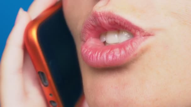 Close-up, vrouwelijke lippen zonder make-up praten over een rode mobiele telefoon, tegen een blauwe achtergrond. 4k, slow-motion — Stockvideo