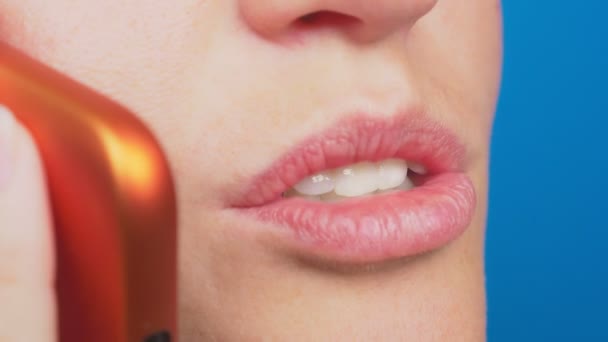 Nahaufnahme, ungeschminkte weibliche Lippen, die auf einem roten Handy vor blauem Hintergrund sprechen. 4k, Zeitlupe — Stockvideo