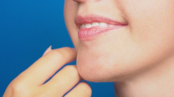 Primer plano, labios de mujer sin maquillaje, la chica toca su cara con su mano. sobre un fondo azul. 4k, cámara lenta — Vídeos de Stock