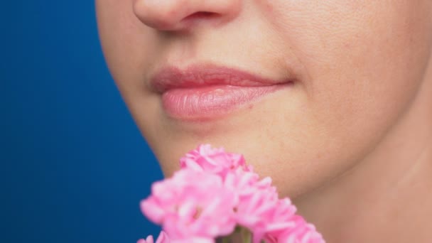 Nahaufnahme, weibliche Lippen ohne Make-up, das Mädchen schnuppert Rosen. auf blauem Hintergrund. 4k, Zeitlupe — Stockvideo