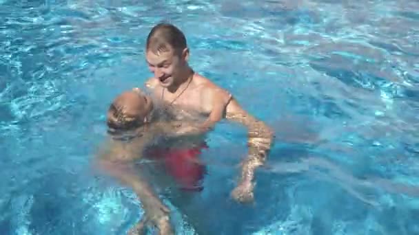 那位年轻的父亲正在教他的小女儿在游泳池里游泳。快乐的女孩和她的父亲笑着玩。4k. 慢动作 — 图库视频影像
