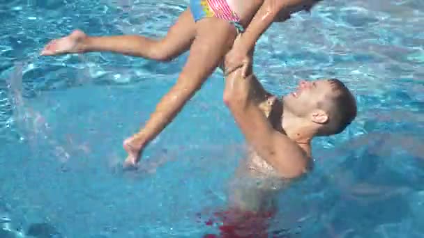 Молодой отец учит свою маленькую дочь плавать в бассейне. Счастливая девушка и ее отец смеются и веселятся. 4k. Медленное движение — стоковое видео