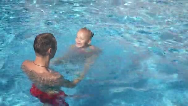 Молодой отец учит свою маленькую дочь плавать в бассейне. Счастливая девушка и ее отец смеются и веселятся. 4k. Медленное движение — стоковое видео