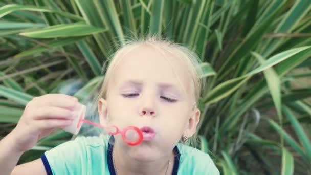Petite fille blonde soufflant des bulles de savon sur un fond de parc tropical. 4k, au ralenti — Video