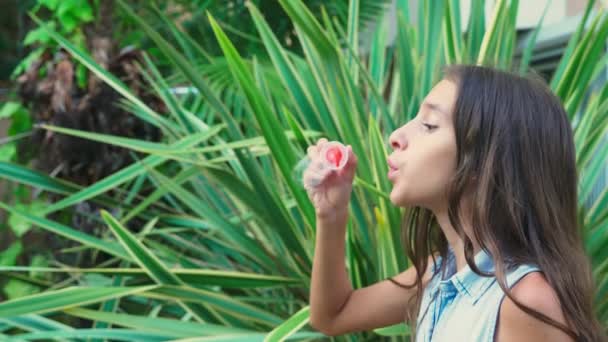 Meisje tiener brunette blazen van zeepbellen tegen de achtergrond van een tropisch park. 4k, slow-motion — Stockvideo