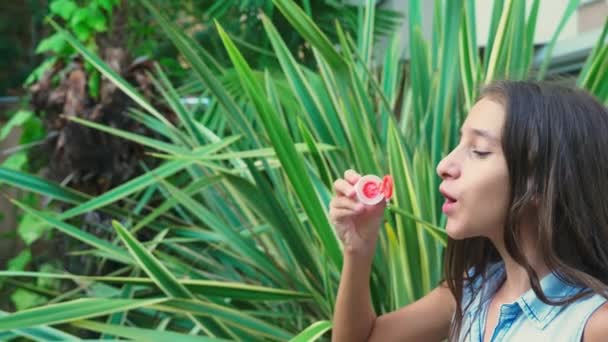 Chica adolescente morena soplando burbujas de jabón contra un fondo de parque tropical. 4k, cámara lenta — Vídeos de Stock