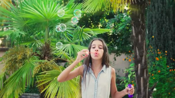 女孩青少年黑发吹肥皂泡沫反对热带公园背景。4k. 慢动作 — 图库视频影像