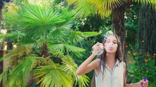 Fille adolescent brunette soufflant des bulles de savon sur un fond de parc tropical. 4k, au ralenti — Video