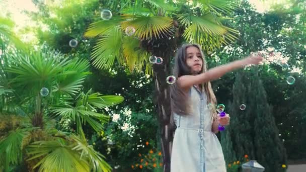 Two girls, brunette and blond blowing soap bubbles against a tropical park background. 4k, slow motion — Stock Video