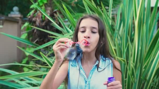 Ragazza adolescente bruna soffiando bolle di sapone contro uno sfondo del parco tropicale. 4k, rallentatore — Video Stock