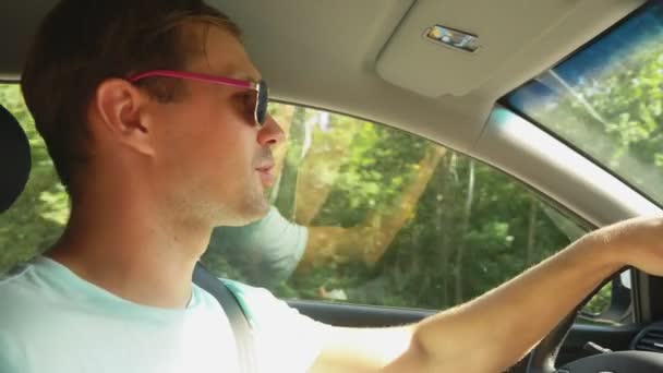 Um jovem bonito de óculos de sol, a conduzir um carro. Conduzir de férias, natureza. 4k, câmera lenta — Vídeo de Stock