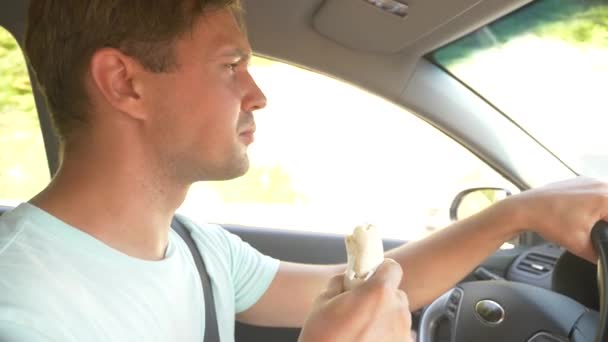 O homem ao volante do carro, come fast food, enquanto o carro está se movendo. num dia ensolarado de verão. 4k, câmera lenta — Vídeo de Stock