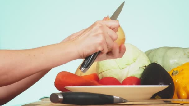 Una mano femenina se corta con un cuchillo una cebolla. mezcla de verduras para cocinar estofado de verduras. color de fondo. 4k, el concepto de alimentación saludable y cosecha . — Vídeos de Stock