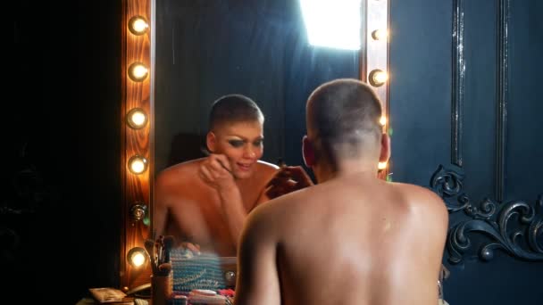 Концепция пародийного макияжа. красивый молодой человек наносит макияж на лицо, сидя перед зеркалом в гримерке. профессиональный художник пародии. макро, 4k . — стоковое видео