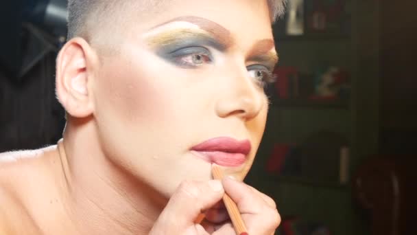 Koncept parodie make-up. pohledný mladý muž platí make-upu na obličeji sedí před zrcadlem v šatně. profesionální travesti umělec. detail, 4k. — Stock video