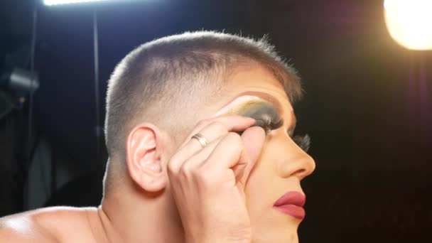 Koncept parodie make-up. pohledný mladý muž platí make-upu na obličeji sedí před zrcadlem v šatně. profesionální travesti umělec. detail, 4k. — Stock video