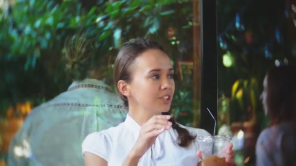Dos novias beben cócteles a través de una paja, sentado en un café al aire libre de verano. 4k — Vídeos de Stock