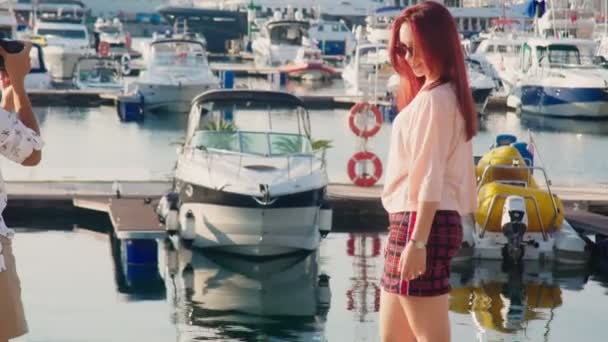 Girl photographer takes pictures of a model on a sea dock on the background of yachts. 4k. — Stock Video