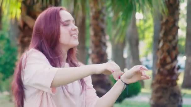 Красивая девушка-подросток с рыжими волосами танцует в парке на фоне пальм. 4k, крупный план — стоковое видео