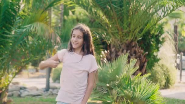 Όμορφο εφηβικό κορίτσι που χορεύει στο πάρκο σε ένα φόντο από φοίνικες. 4k — Αρχείο Βίντεο
