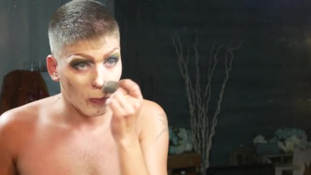 Concepto de maquillaje parodia. un joven guapo se pone maquillaje en la cara, sentado frente a un espejo en el vestidor. artista travesti profesional. primer plano, 4k . — Vídeo de stock