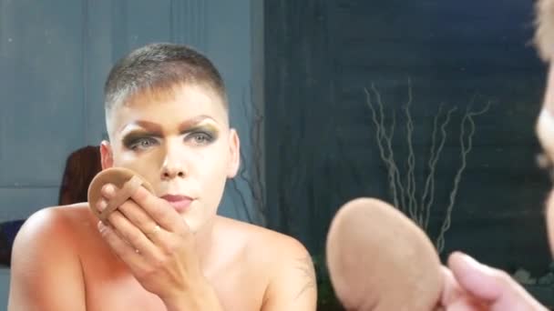 Концепция пародийного макияжа. красивый молодой человек наносит макияж на лицо, сидя перед зеркалом в гримерке. профессиональный художник пародии. макро, 4k . — стоковое видео