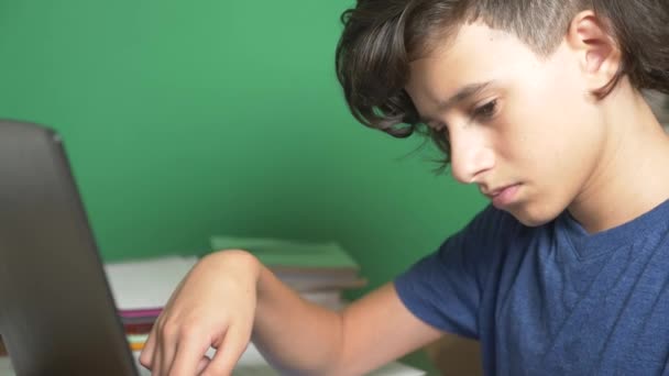 Perfil de un adolescente, sobre un fondo verde. Primer plano. el chico se está concentrando en la pantalla del portátil y tomando notas en la tétrada. 4k, cámara lenta . — Vídeos de Stock