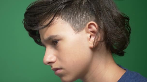 Profile of a teenager boy, on a green background. close-up. the boy is concentrating on the laptop screen and making notes in the tetrad. 4k, slow motion. — Stock Video