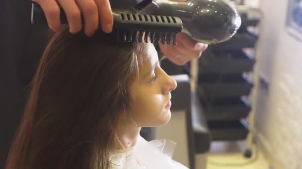 Nahaufnahme, professioneller Friseur. Prozess der Bemalung der Haare eines brünetten Mädchens mit einem Stärkungsmittel für die Haare. Föhnen der Haare mit einem Haartrockner, Zeitlupe — Stockvideo