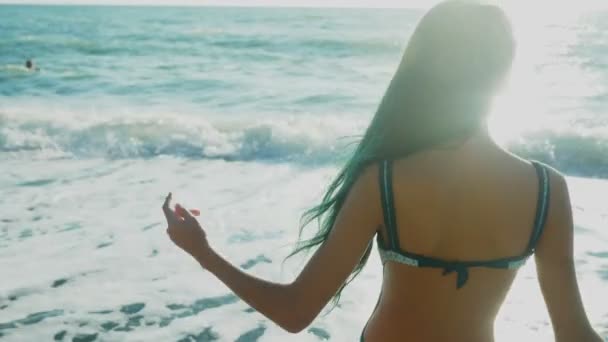 Schöne brünette Mädchen mit langen blauen Haaren, die sich im Wind entwickeln, vor dem Hintergrund von Meereswellen während eines Sturms. Freiheit, Kreativität, Geheimnis. 4k, Zeitlupe — Stockvideo