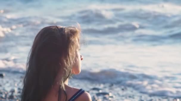 Bela menina morena com cabelos azuis longos, desenvolvendo-se no vento, contra um fundo de ondas do mar durante uma tempestade. liberdade, criatividade, mistério. 4k, câmera lenta — Vídeo de Stock