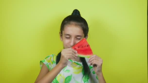 Kedves vidám lány eszik egy görögdinnye, sárga háttéren. 4k, lassú mozgás — Stock videók