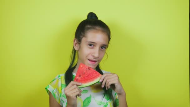 Encantadora chica alegre comiendo una sandía, sobre un fondo amarillo. 4k, cámara lenta — Vídeos de Stock