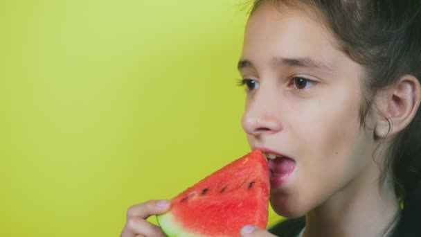 Linda menina alegre comendo uma melancia, em um fundo amarelo. 4k, câmera lenta, close-up . — Vídeo de Stock