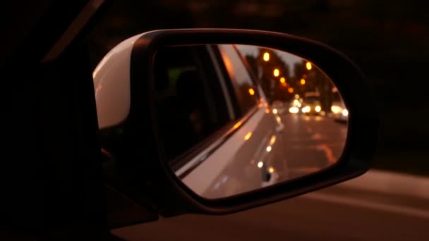 Conduciendo de noche. La vista desde el coche en el espejo retrovisor lateral mientras conduce a través de la ciudad nocturna. luces borrosas de la ciudad. 4k — Vídeos de Stock