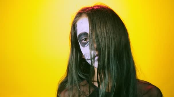 Halloween dívka s make-up kostra na polovinu tváře, oblečený jako čarodějnice, Pózování na světle žlutém podkladu. 4 k, Zpomalený, detail — Stock video