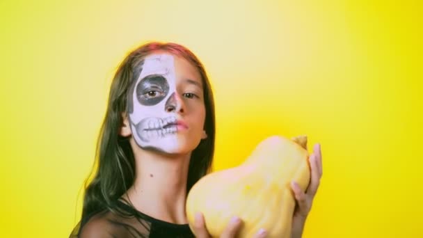 Halloween, menina com esqueleto de maquiagem na metade do rosto, vestida de bruxa, posando em fundo amarelo brilhante. 4k, câmera lenta, close-up — Vídeo de Stock