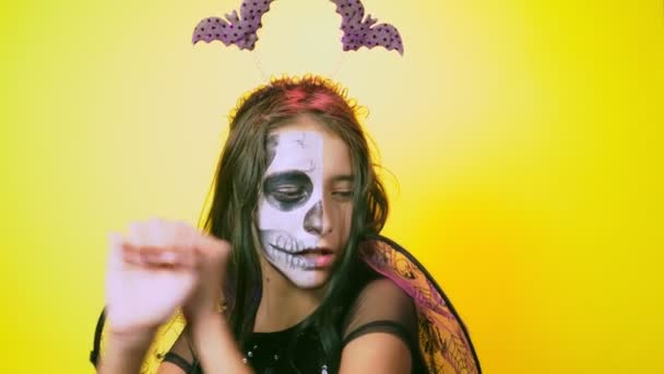 Halloween, girl with make-up skeleton on half face, dressed as witch, posing on bright yellow background. 4k, slow-motion, close-up — Stock Video