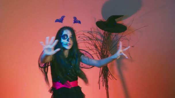 Halloween, chica con esqueleto de maquillaje en media cara, vestida de bruja, posando y bailando sobre un fondo rojo. 4k, cámara lenta — Vídeo de stock