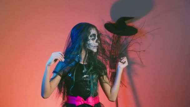Halloween, Mädchen mit Schminkskelett auf dem halben Gesicht, als Hexe verkleidet, posierend und tanzend auf rotem Hintergrund. 4k, Zeitlupe — Stockvideo