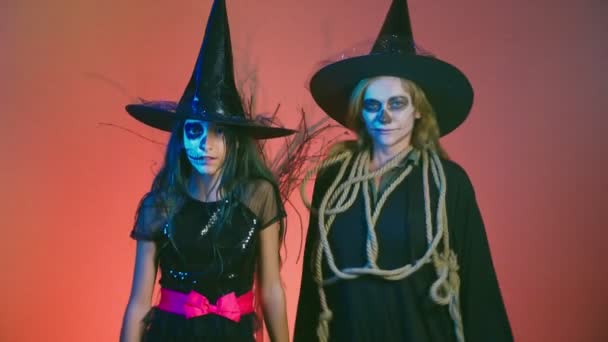 Halloween, une fille maquillée, un squelette pour la moitié du visage et sa mère, habillée comme des sorcières, posant et dansant sur un fond rouge. 4k, au ralenti — Video