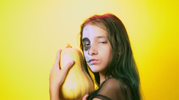 Halloween, menina com esqueleto de maquiagem na metade do rosto, vestida de bruxa, posando em fundo amarelo brilhante. 4k, câmera lenta, close-up — Vídeo de Stock