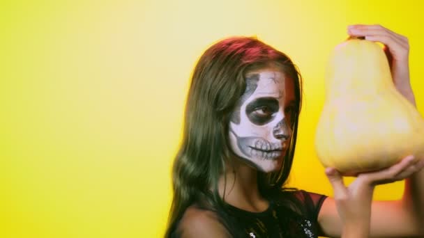 Απόκριες, κορίτσι με μακιγιάζ σκελετού στο μισό πρόσωπο, ντυμένος σαν μάγισσα, θέτοντας σε φωτεινό κίτρινο φόντο. 4 k, αργή κίνηση, γκρο πλαν — Αρχείο Βίντεο