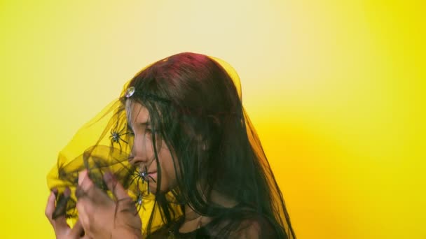 Halloween, chica con esqueleto de maquillaje en media cara, vestida de bruja, posando sobre un fondo amarillo brillante. 4k, cámara lenta, primer plano — Vídeo de stock