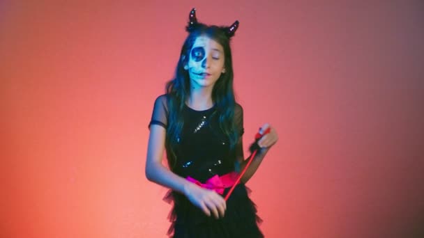 Хеллоуїн, дівчина з макіяжним скелетом на половині обличчя, одягнена як відьма, позує і танцює на червоному тлі. 4k, повільний рух — стокове відео