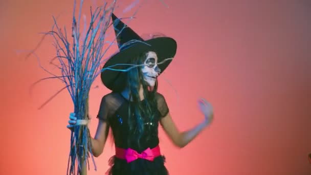 Halloween, chica con esqueleto de maquillaje en media cara, vestida de bruja, posando y bailando sobre un fondo rojo. 4k, cámara lenta — Vídeos de Stock