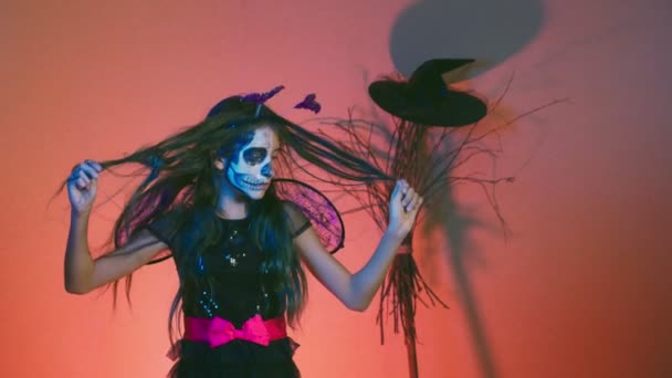 Halloween, chica con esqueleto de maquillaje en media cara, vestida de bruja, posando y bailando sobre un fondo rojo. 4k, cámara lenta — Vídeo de stock