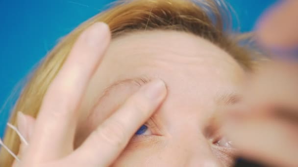Extremo close-up. arrancando pinças de sobrancelhas, uma menina loira com olhos azuis puxa cabelos desnecessários de sua sobrancelha, câmera lenta . — Vídeo de Stock