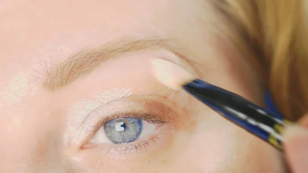 Super close-up, uma mulher fazendo sua maquiagem olho, pinta a pálpebra com sombras . — Fotografia de Stock