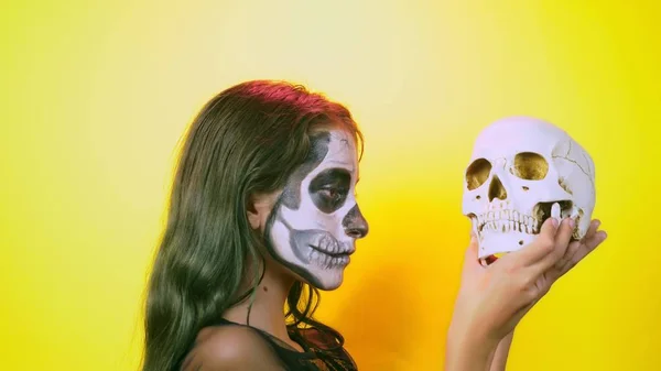 Halloween, menina com esqueleto de maquiagem na metade do rosto, vestida de bruxa, posando em fundo amarelo brilhante. close-up — Fotografia de Stock